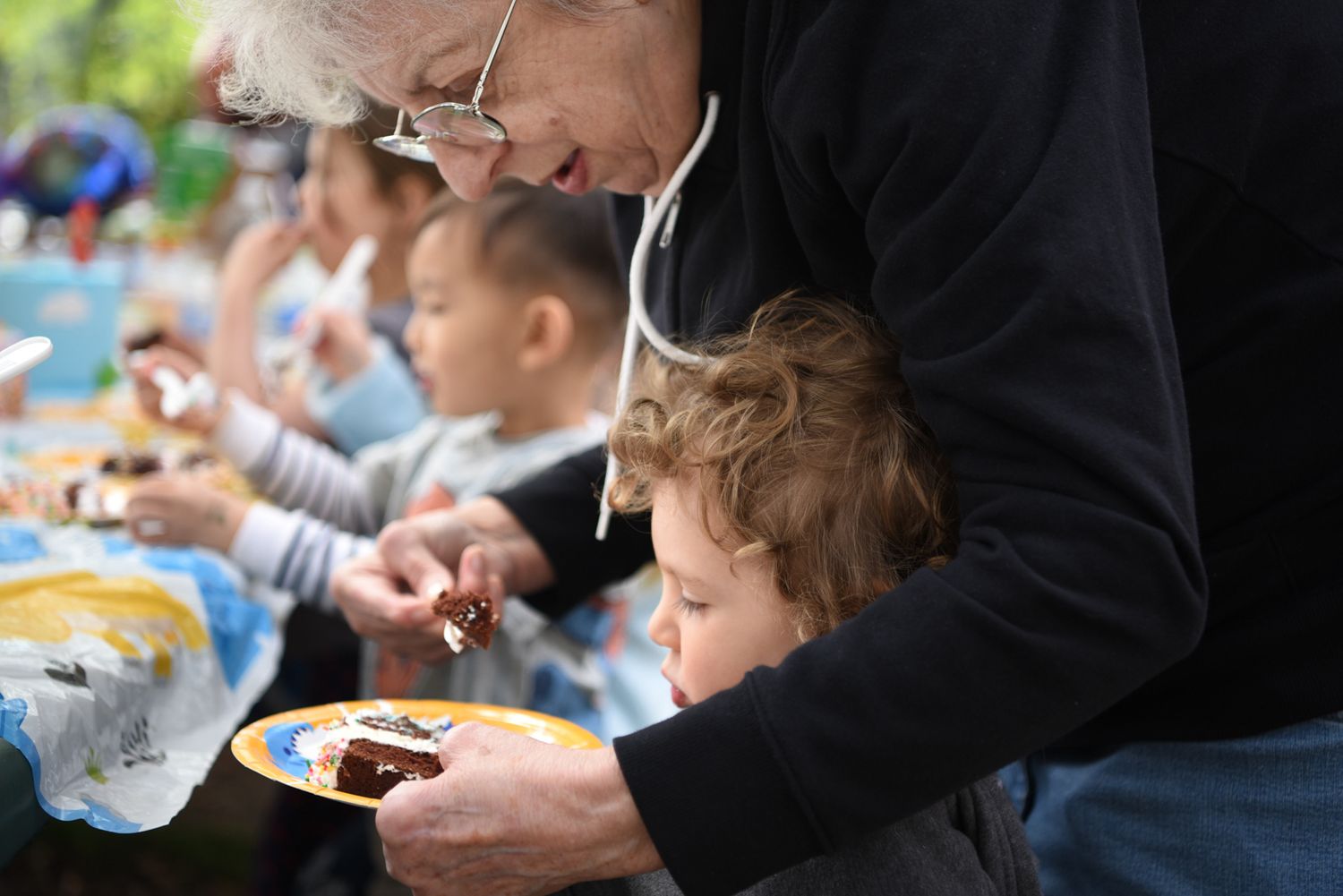 Birthday party, grandma and toddler, with plates and drinks on the table.