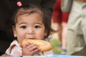 A young child takes a bite of a  bun at a birthday party.