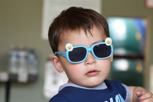 A small child wearing bright blue sunglasses and a navy shirt poses indoors. Birthday party photo.