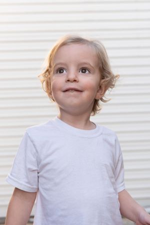 A small child smiles while looking up against a white striped background.
