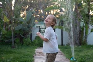 A toddler joyfully playing in a backyard sprinkler on a summer day.