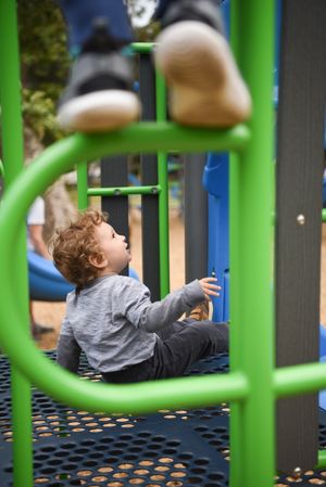 Young child plays on colorful playground equipment at an outdoor park in the sunshine at a birthday party.