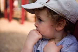 A thoughtful toddler in a baseball cap with hand on chin in an outdoor setting. Children's birthday photography Pasadena.