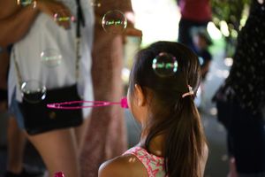 Child blowing soap bubbles which are floating in the air at an outdoor gathering.