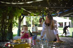 Mom a daughter enjoy an outdoor activity at a covered picnic area with crafts and supplies on the table  at a birthday party.