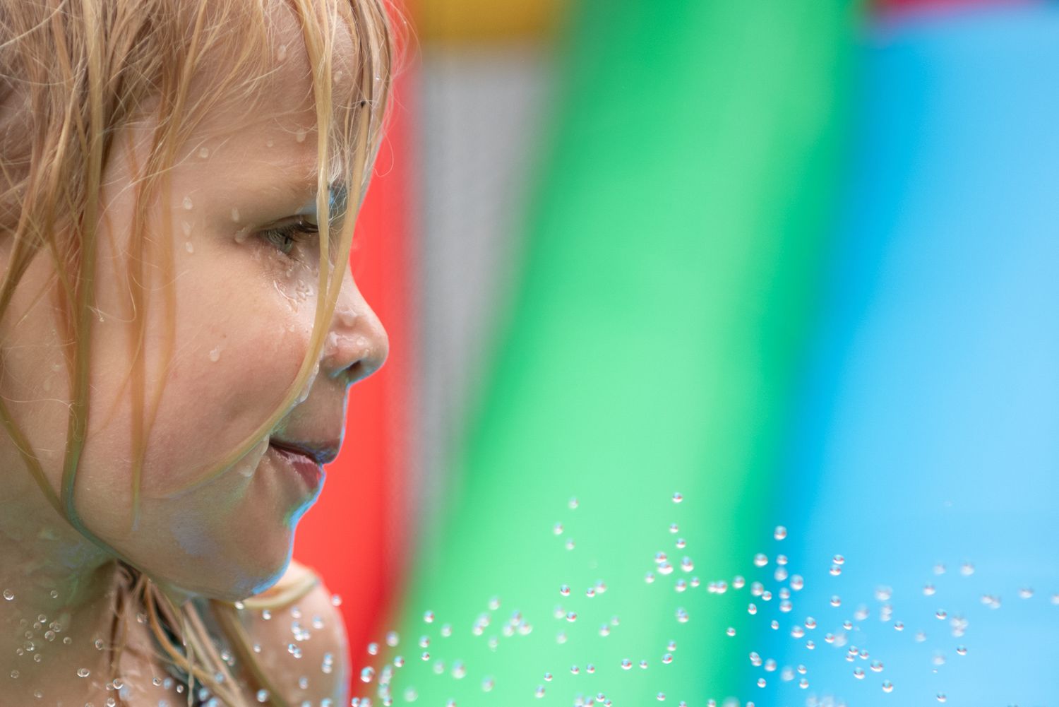 A profile view of a young child with light hair against a colorful blurred background with sparkles at a birthday party.
