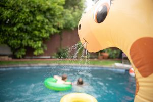 Water spraying from an inflatable giraffe pool toy into a swimming pool with floats during a birthday party.