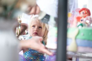 A child seen through a blurred foreground with birthday cake visible in a colorful background.