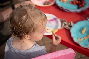 Children eating and enjoying a meal together at a red table with bright blue plates at a birthday party.