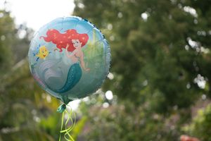 A Disney Little Mermaid themed balloon floats outdoors against a green blurred background.