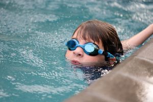 Kid in swimming pool is wearing goggles on a birthday party.