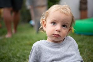 A toddler making different expressions outdoors on a birthday party.