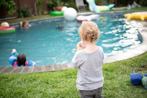 Child in  watches colorful pool floats in backyard swimming pool on summer day birthday party.