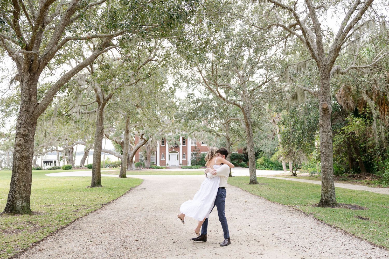 Man spinning his fiancee around after proposing to her in front of a historic mansion.