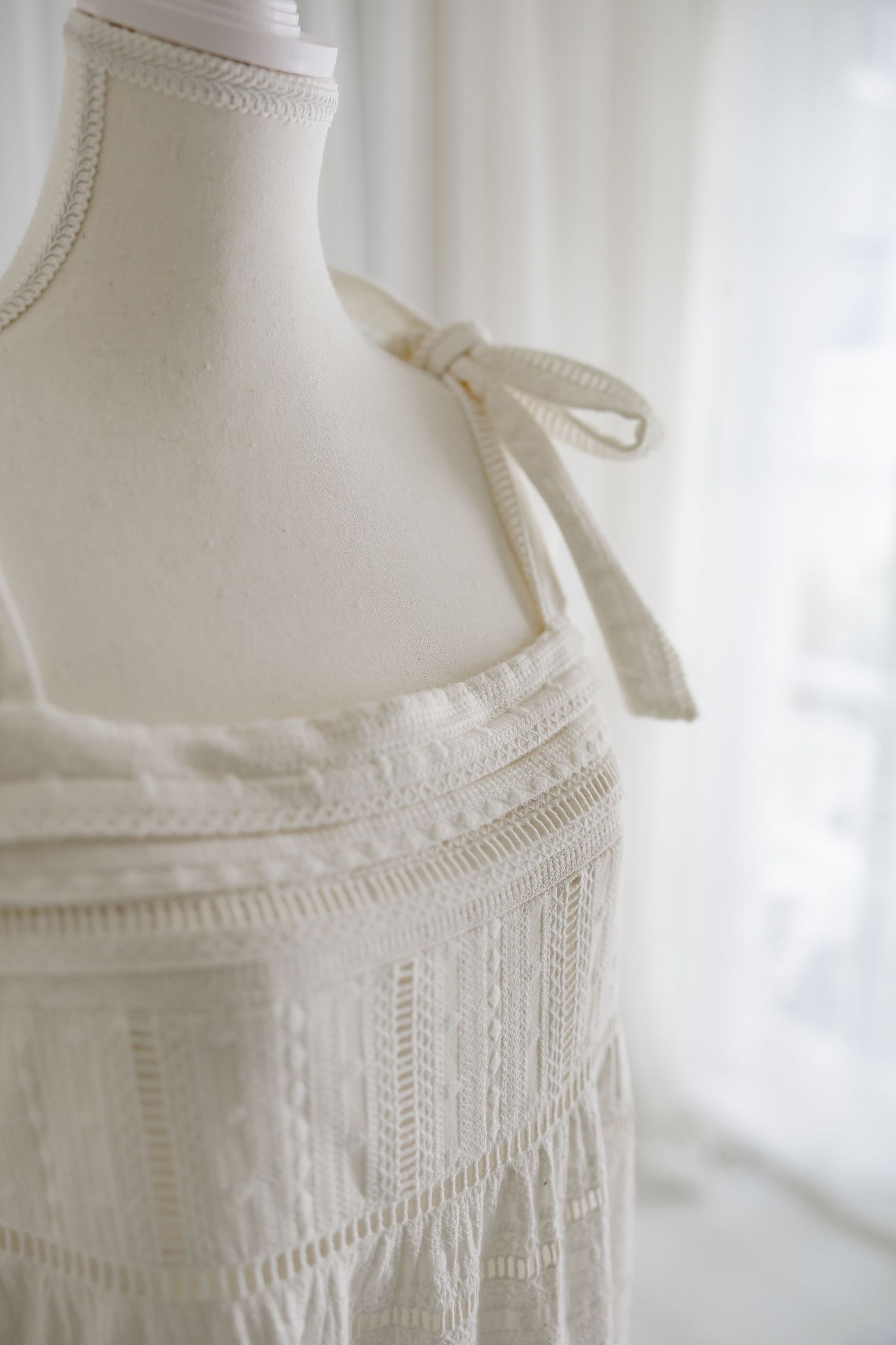 Detailed view of white dress bodice showing delicate pintucks and ribbon shoulder straps.