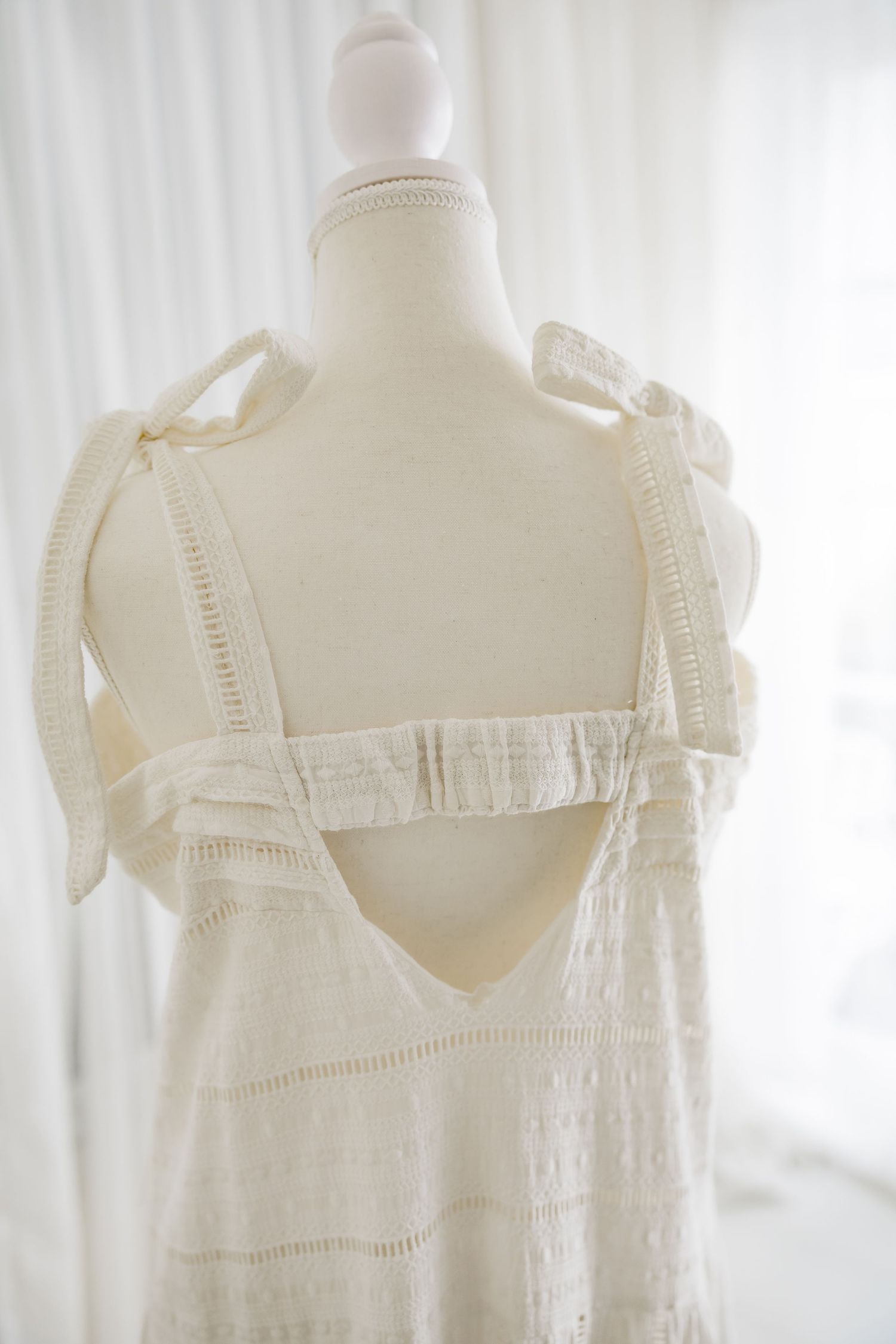 Back view of white cotton dress showing open back design with ribbon ties.