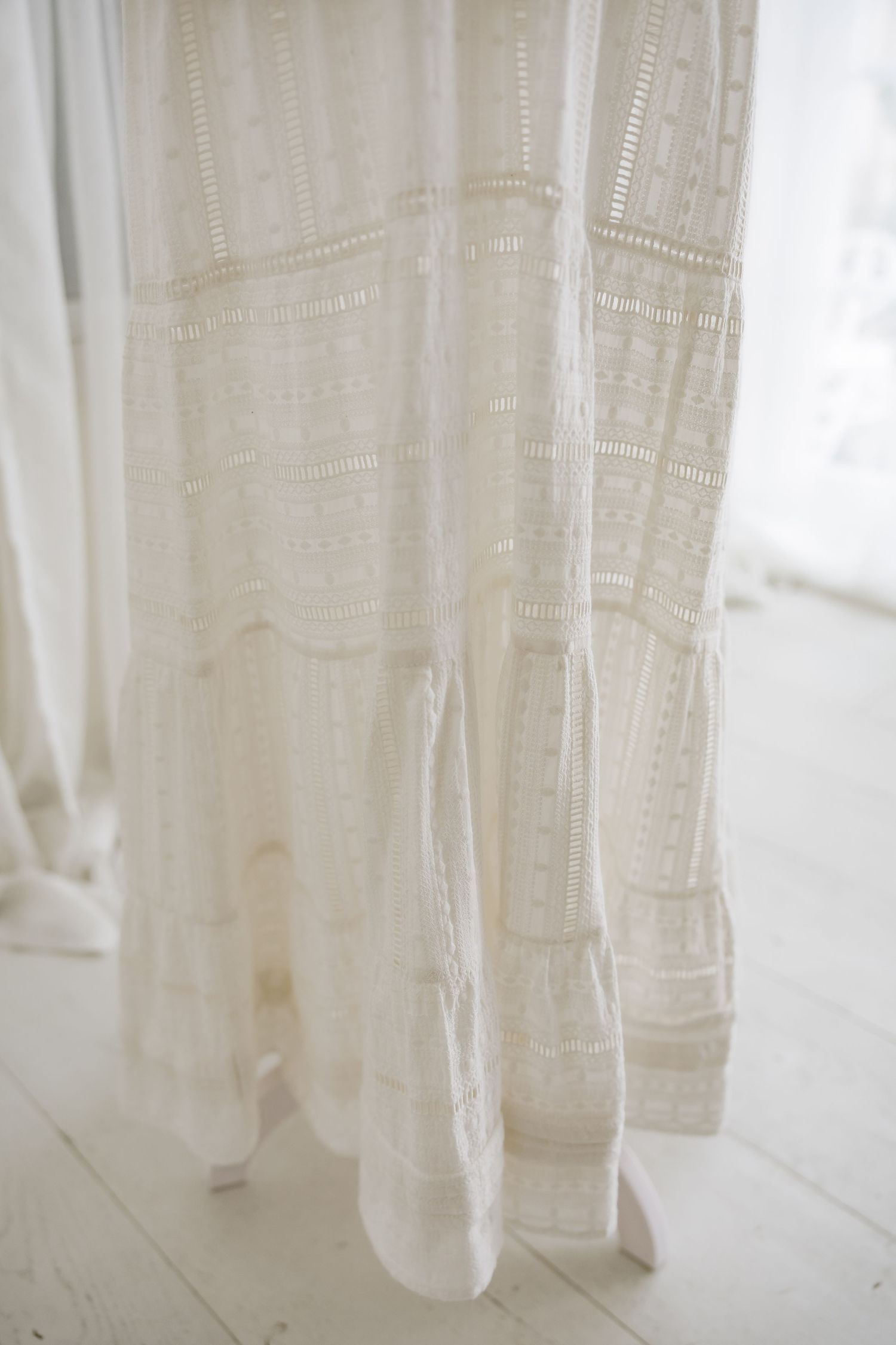 Flowing white cotton dress skirt with vertical lace insets photographed against light background.