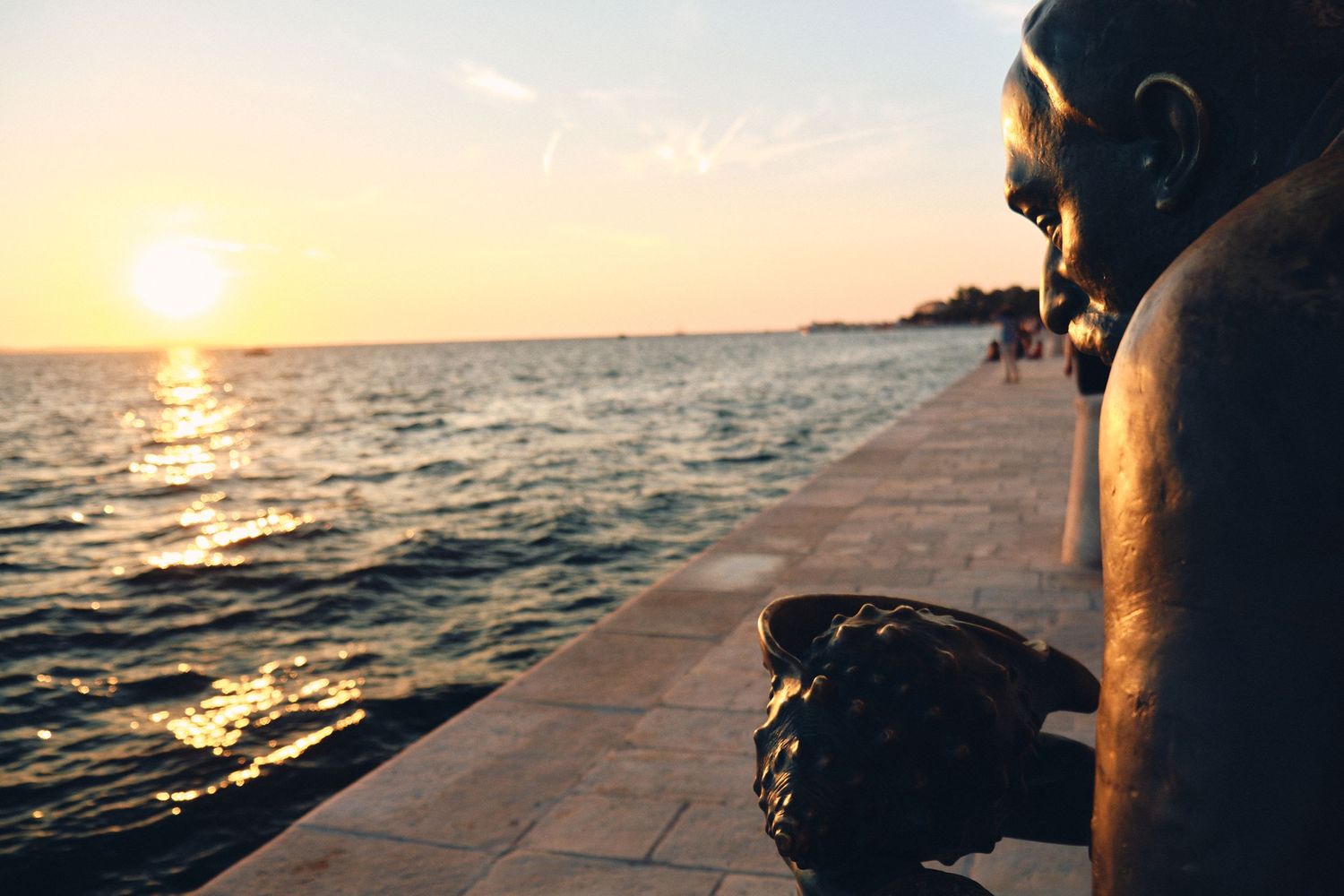 Sunset silhouette of person sitting on seaside promenade watching the horizon.