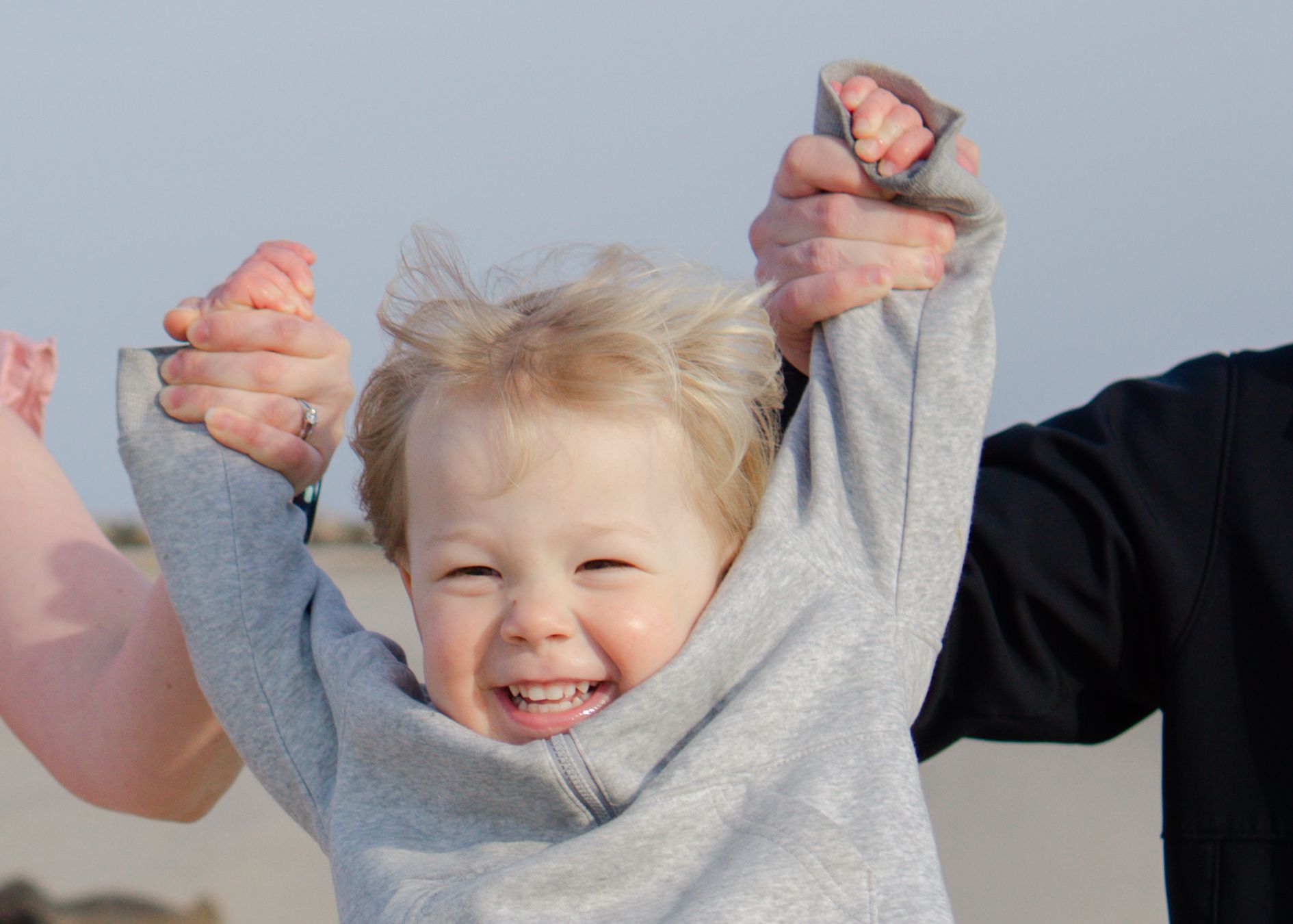 Carefree childhood moment, child with raised arms soaring above parent’s hands.