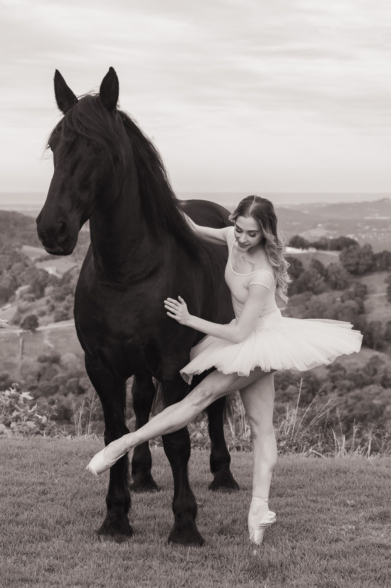 Black and white portrait with ballet dancer and majestic black horse on hillside.