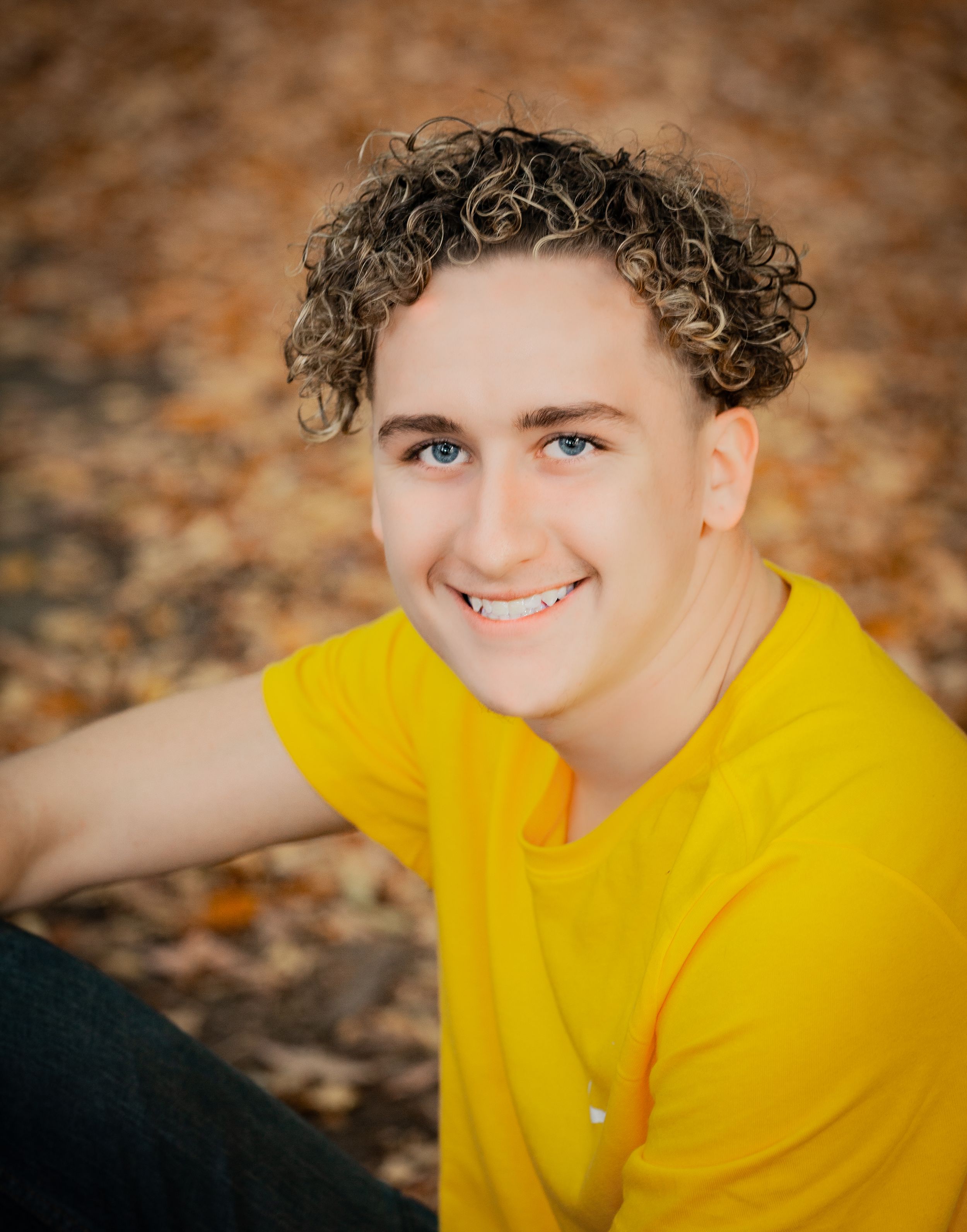 Person in bright yellow shirt smiling against autumn foliage background.