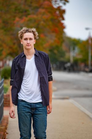 Casual fall portrait on sidewalk with autumn trees in background.