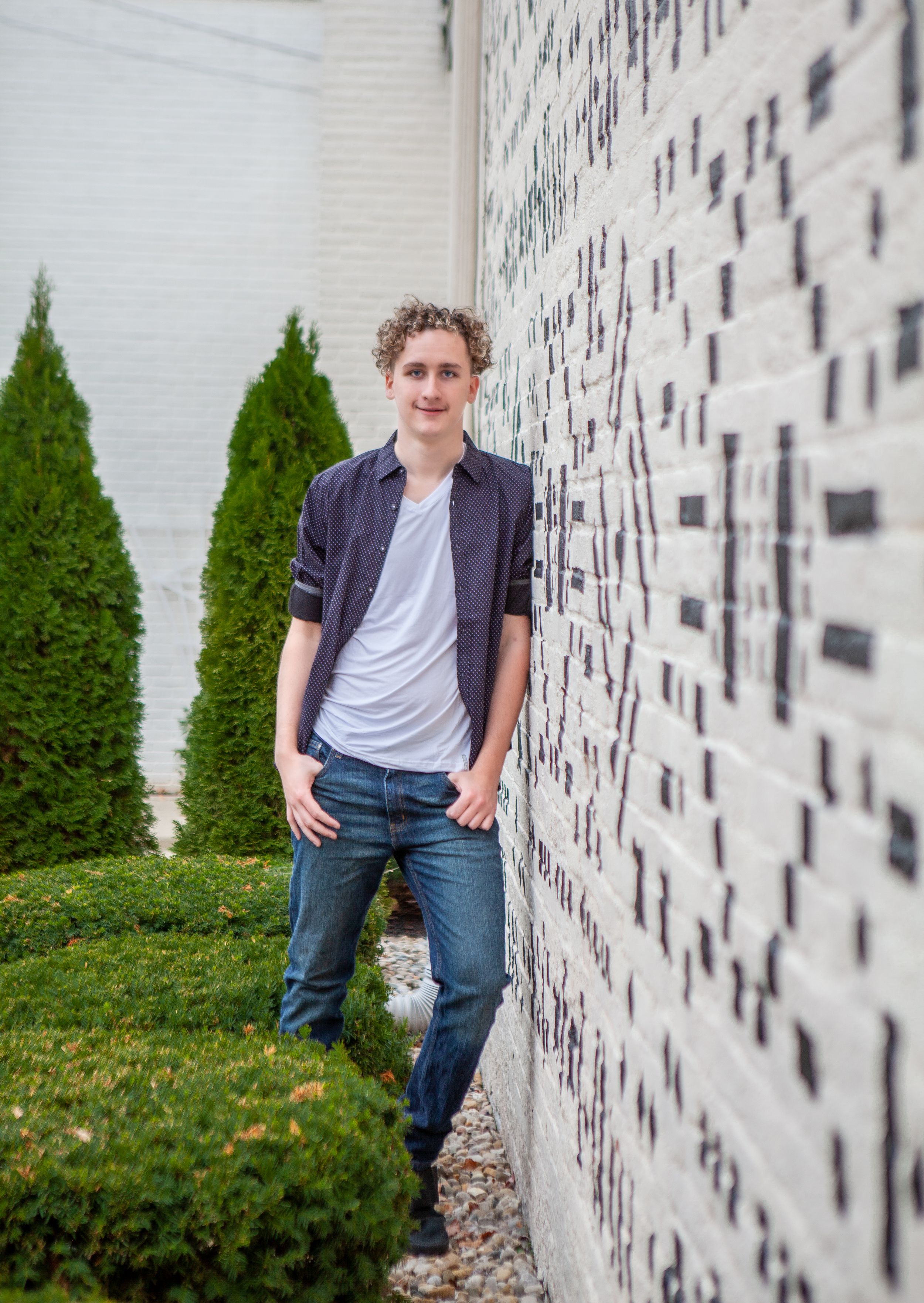 Person leaning against white textured wall with decorative pattern and green shrubs.