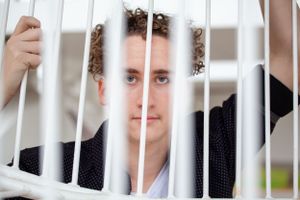 Portrait through white vertical bars showing curly hair and a polka dot shirt.