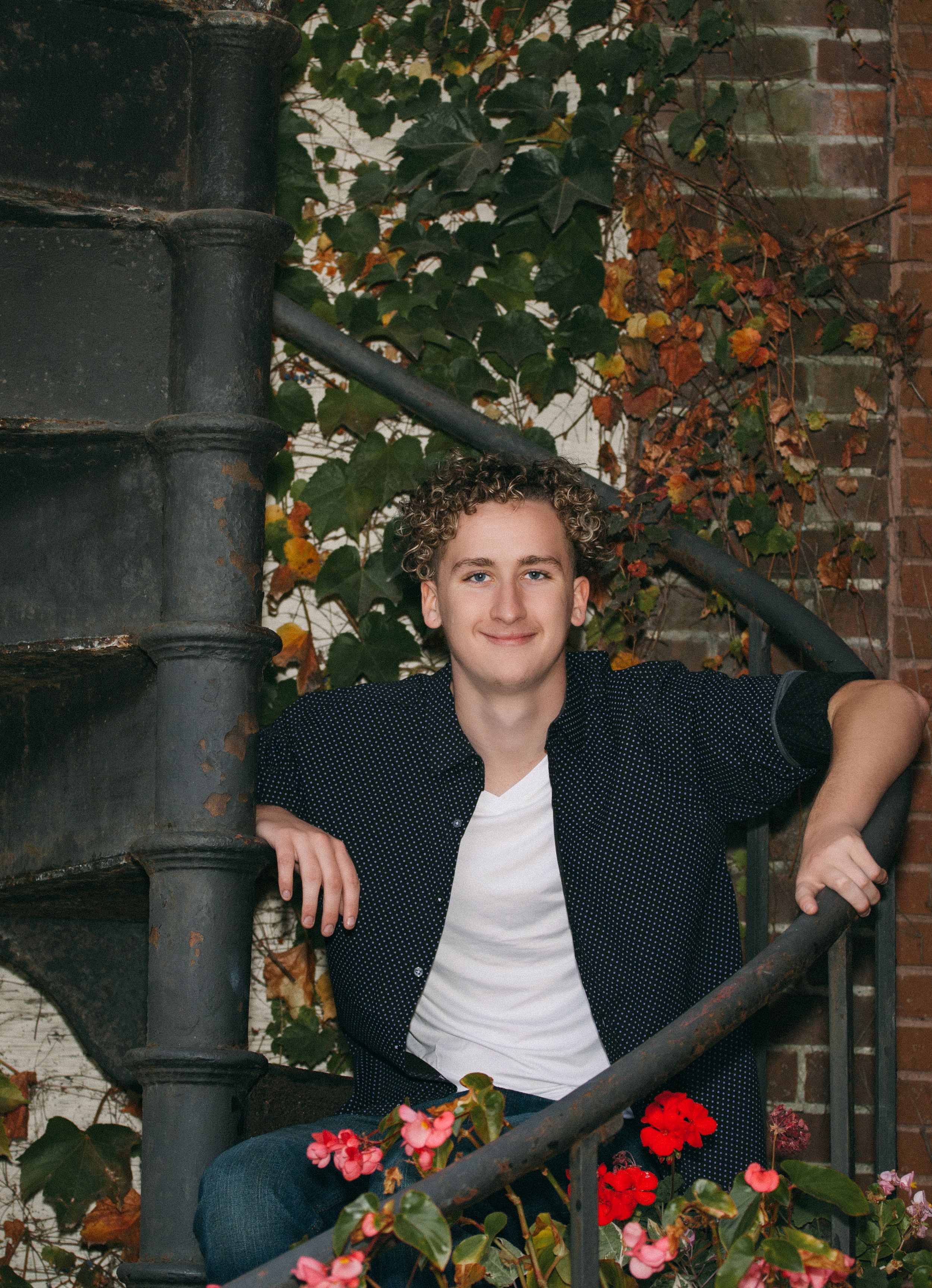 Autumn portrait on spiral staircase with red flowers and ivy covered brick wall.