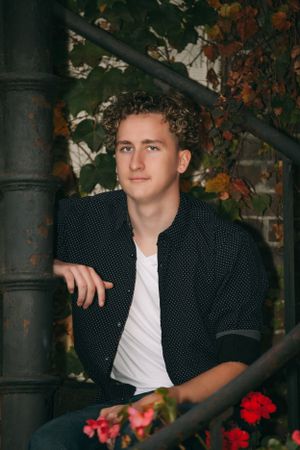 Portrait by vintage metal staircase with fall foliage and red flowers.