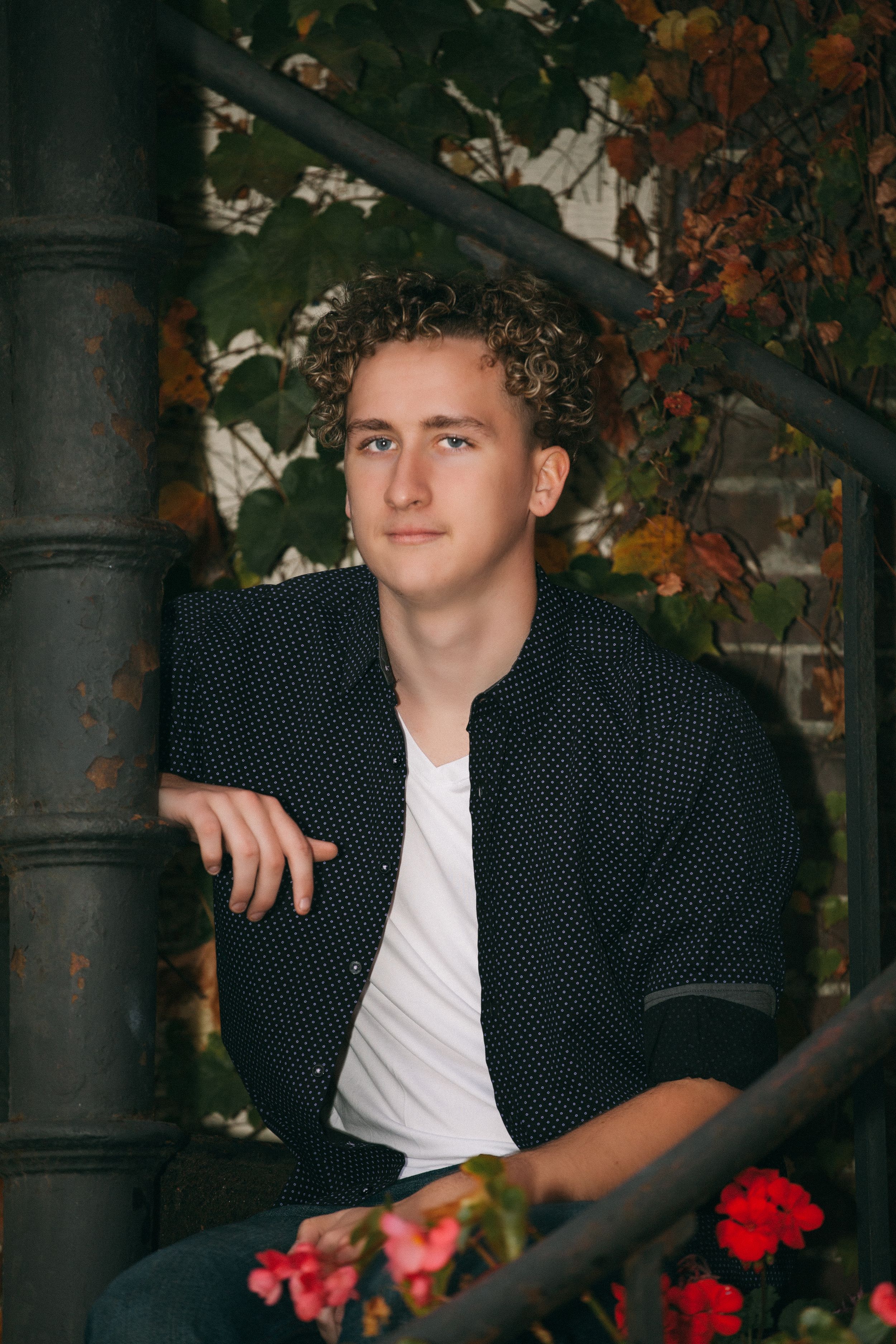 Portrait by vintage metal staircase with fall foliage and red flowers.