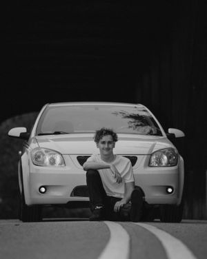 Creative black and white photo with person peeking between two white cars.