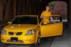 Bright yellow sports car with open door under wooden covered bridge.