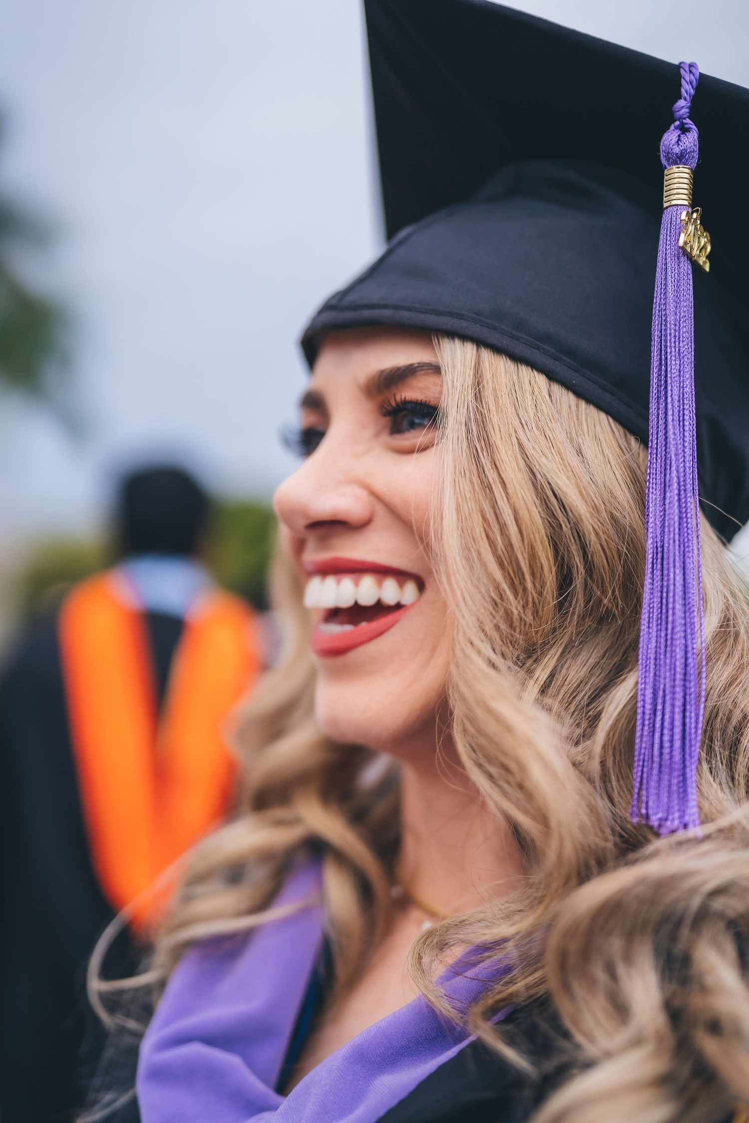 Graduate wearing a black cap with purple tassel smiles during commencement ceremony.