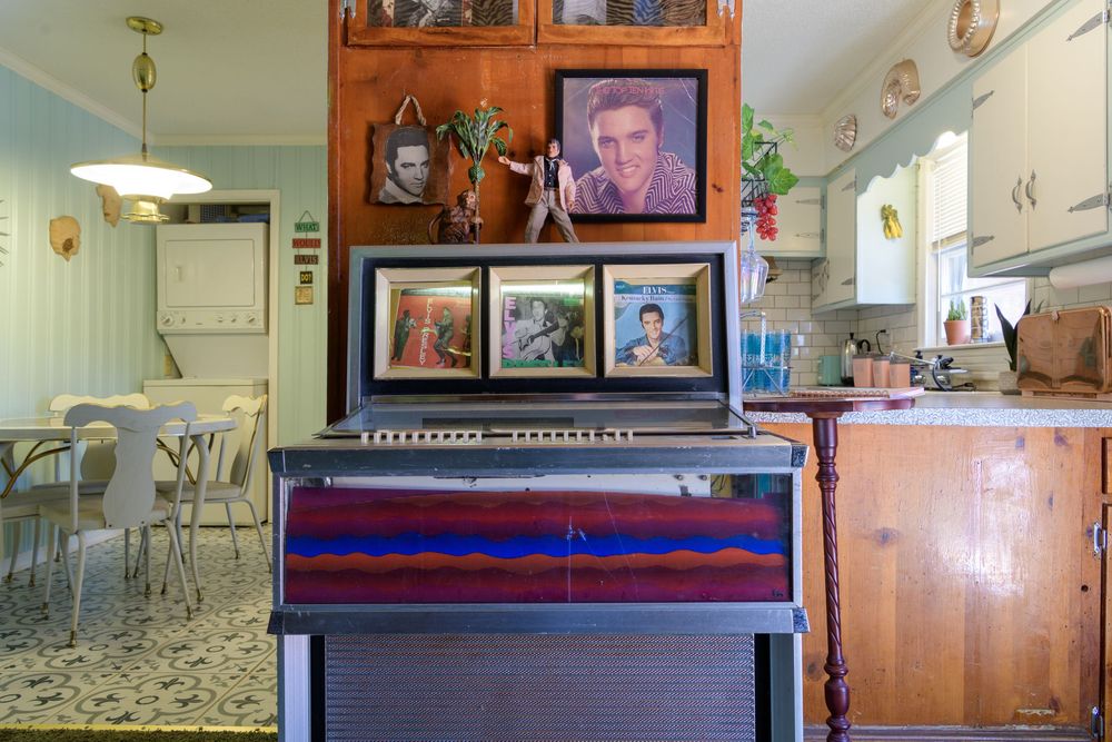 A retro-styled kitchen interior with a vintage jukebox, framed photographs on wood cabinets, and diner-style seating.