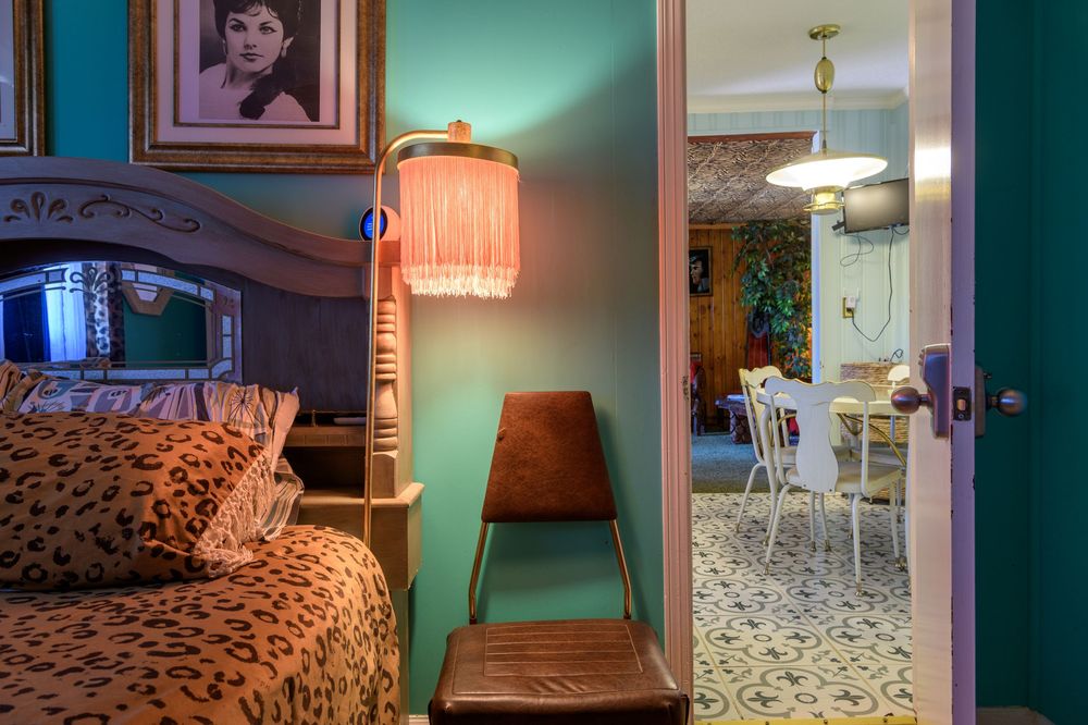 Interior view showing bedroom with leopard print bedding, vintage lamp, and dining area visible through doorway.