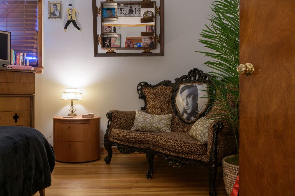A cozy corner featuring an ornate vintage settee, round side table with lamp, and decorative wall art in a warm-lit room.