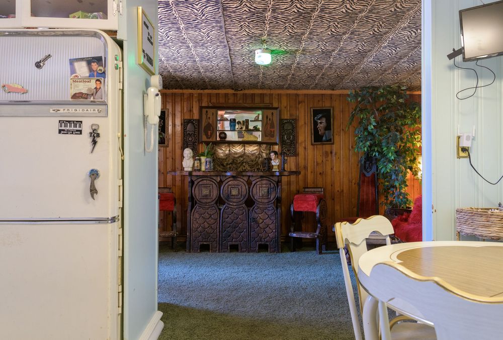 Interior view showing a doorway between rooms with wooden paneling, vintage decor and a red chair visible in the background.