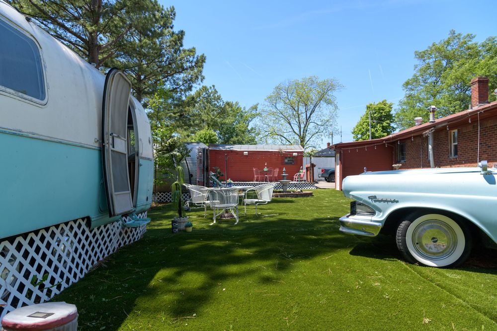 Vintage campers and classic cars displayed on a green lawn with a red building in the background.