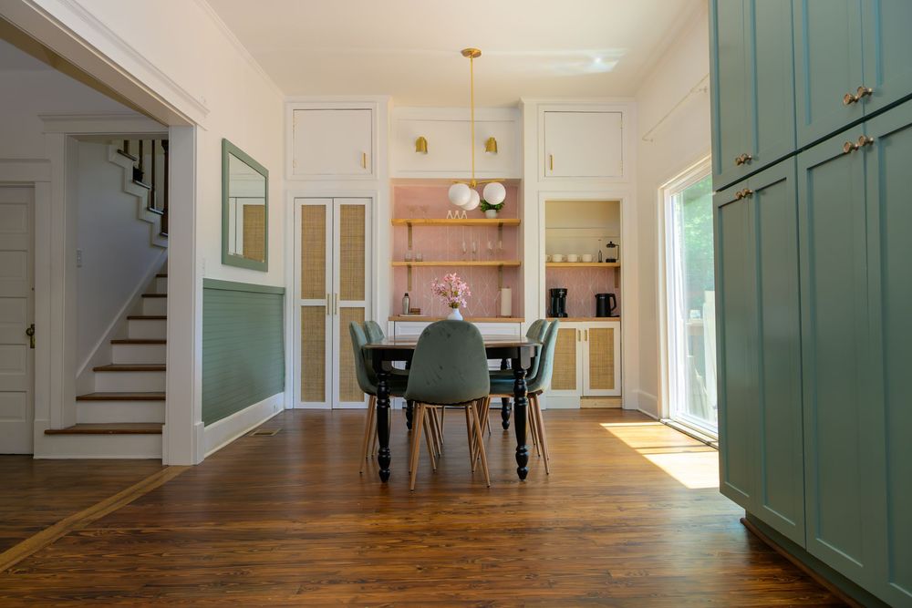 Modern dining room with hardwood floors, sage green cabinets, and pendant lights in an open concept home interior.
