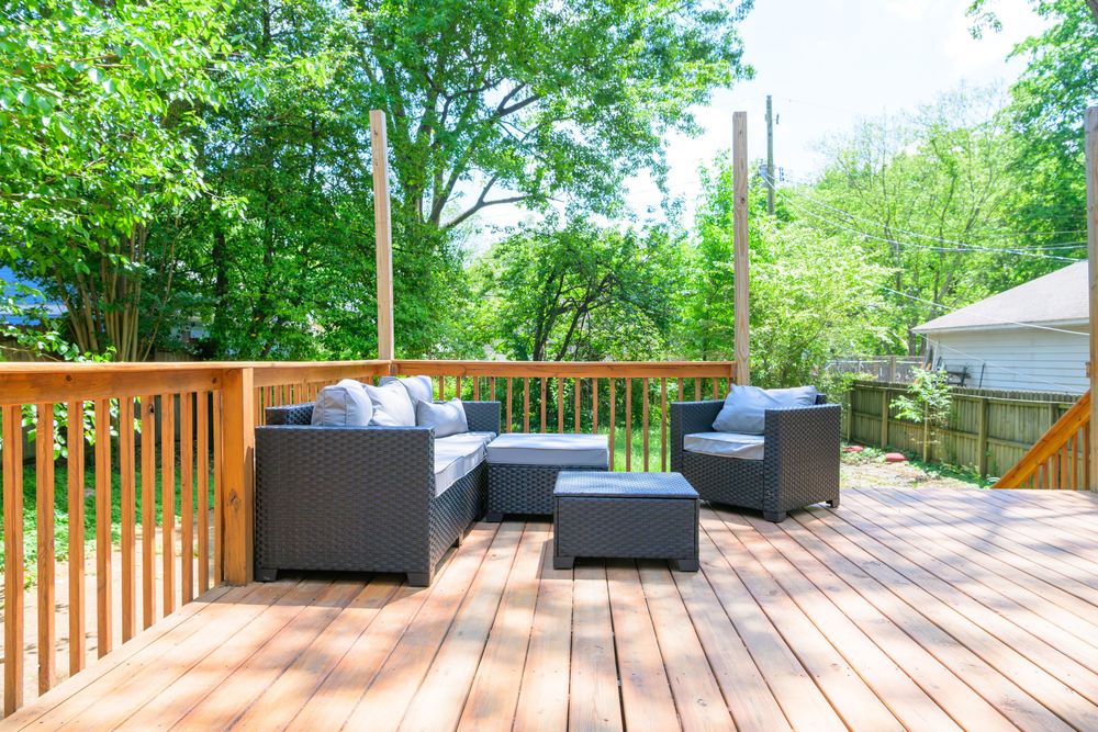 Modern outdoor patio furniture set arranged on a wooden deck surrounded by lush green trees in summer.