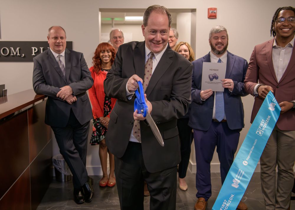 A group of people smile and celebrate in an office hallway while displaying colorful award ribbons.