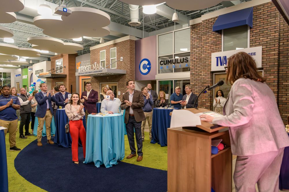 A group of people gathered around high cocktail tables at a networking event in a modern office space with brick walls.
