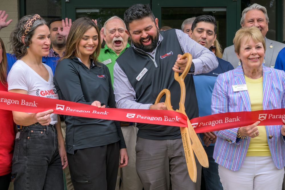 A group of people gather at a ribbon cutting ceremony holding large wooden scissors for a celebratory event.