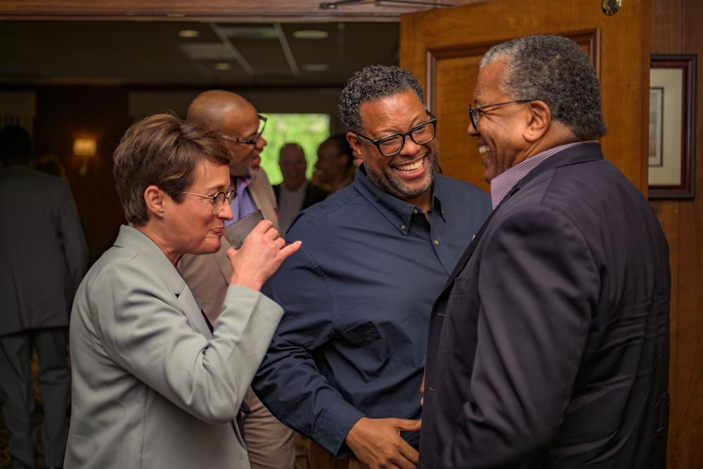 Three people engaged in animated conversation during an indoor gathering or event.