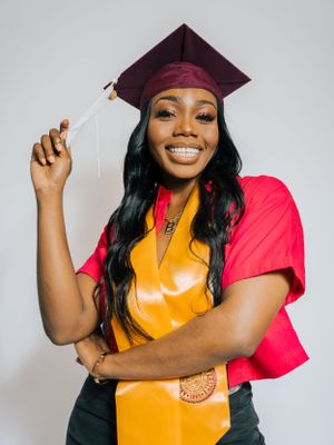 Graduate in burgundy cap and gold stole celebrates with bright smile.
