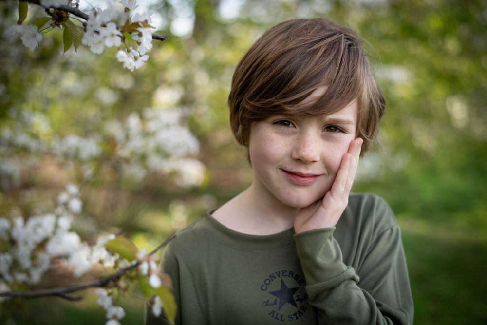 Young person in olive green shirt poses near blooming spring flowers.
