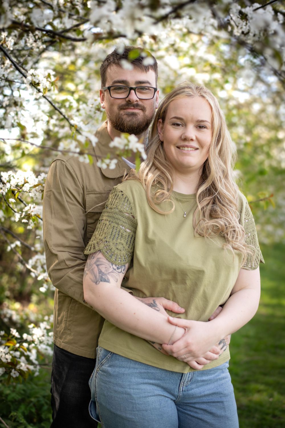 Happy couple embracing under flowering cherry blossom trees in spring garden.
