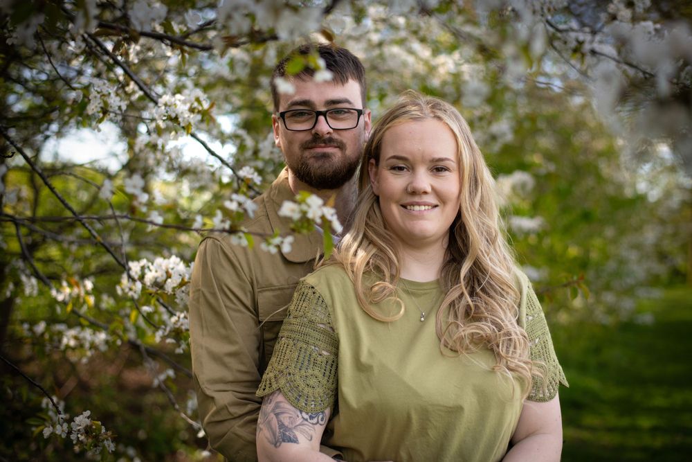Couple posing together under blooming spring tree branches.