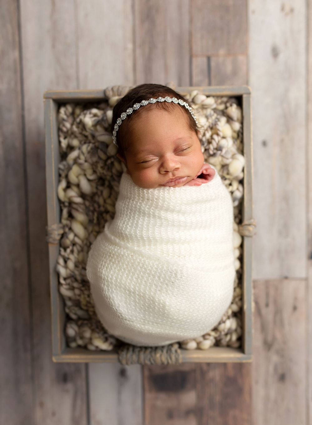 newborn girl wrapped in a cream wrap sleeping in a basket